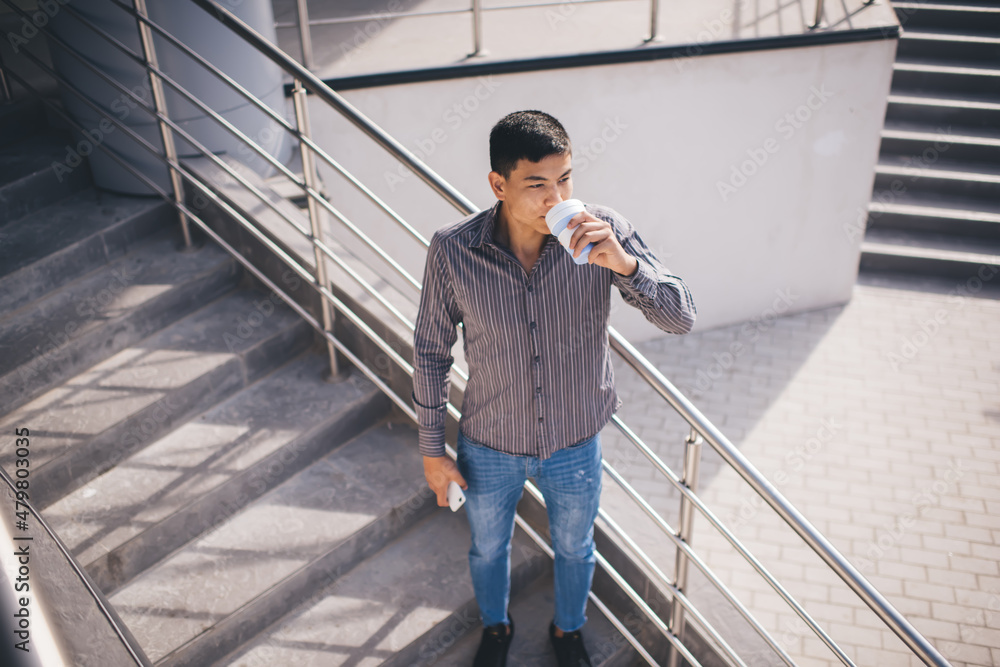 Asian guy with smartphone and coffee on stairs