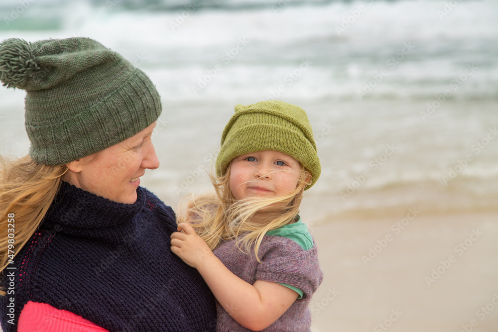 Blonde mother carrying toddler daughter at the beach on a stormy day. Blonde mother carrying toddler daughter at the beach on a stormy day.