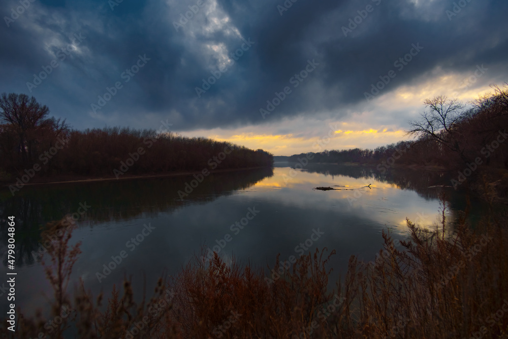 a beautiful autumn landscape in the evening - forest with river and cloudy sky