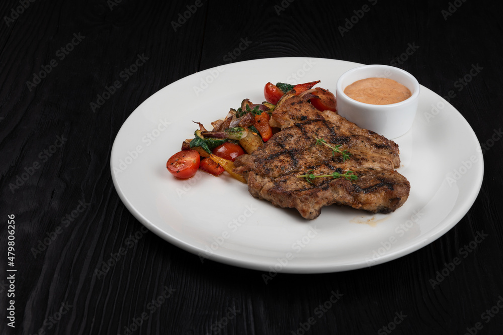 Grilled pork meat steak on white plate on black wooden background