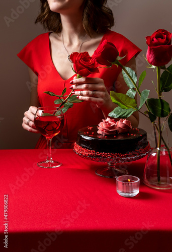 Woman in red dress hand holding a red rose. Romantic candlelight dinner. Valentine's Day. Festive table setting for valentine's day