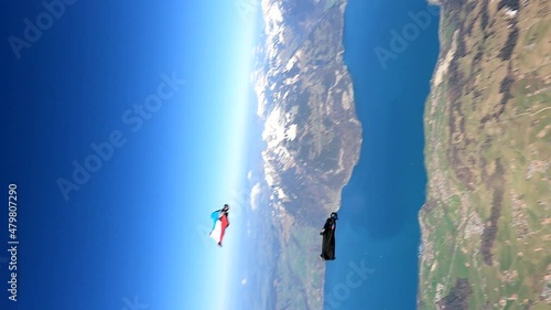 Wingsuit fliers in flight above a mountain lake