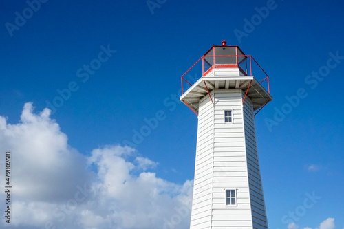 horizontal shot of a lighthouse with white clouds and blue skies in the background on a sunny day