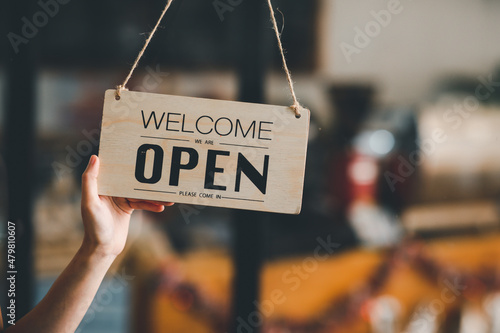 Fototapeta Naklejka Na Ścianę i Meble -  Welcome. Open. barista, waitress woman turning open sign board on glass door in modern cafe coffee shop ready to service, cafe restaurant, retail store, small business owner, food and drink concept