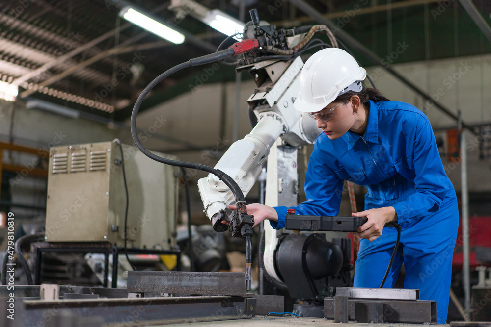 Female automation engineer wear a blue uniform with helmet safety inspection control a robot arm welding machine with a remote system in an industrial factory. Artificial intelligence concept. Female automation engineer wear a blue uniform with helmet safety inspection control a robot arm welding machine with a remote system in an industrial factory. Artificial intelligence concept.