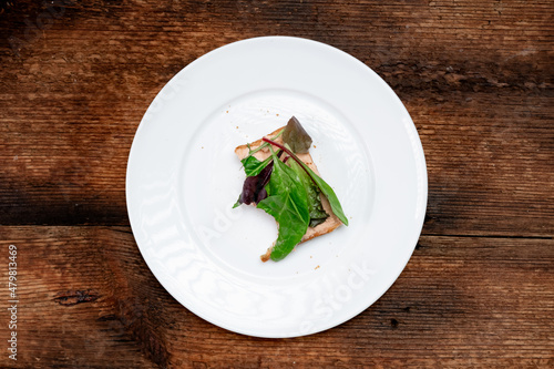 Vegetarian sandwich half eaten. Toast with a creamy spread and assorted edible salad leaves. White plate, dark wooden background. Healthy eating. Food concept.