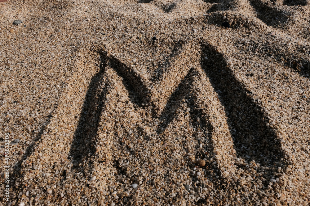 English alphabet. Sand on the beach. The letter M - obrazy, fototapety, plakaty 