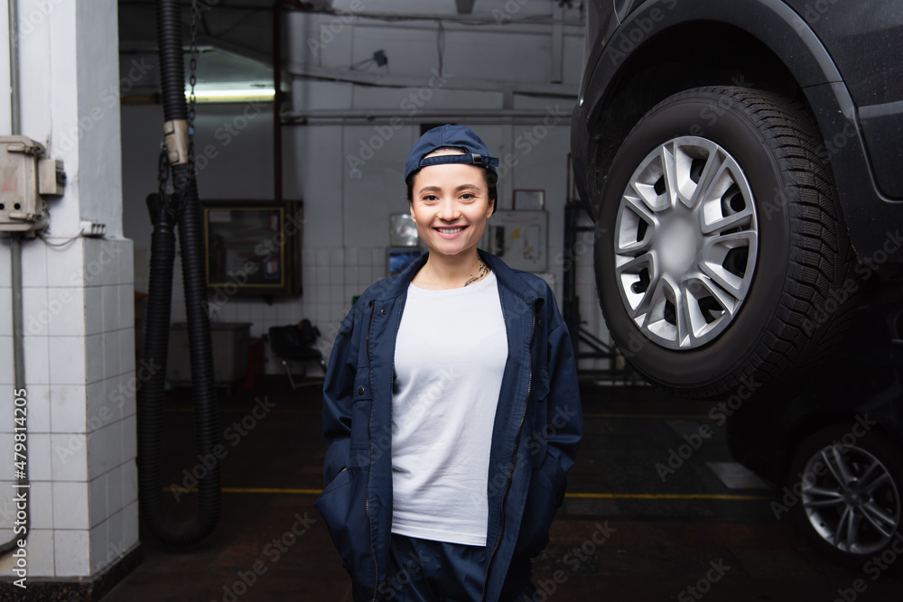 Smiling mechanic looking at camera near car in garage. Smiling mechanic looking at camera near car in garage.