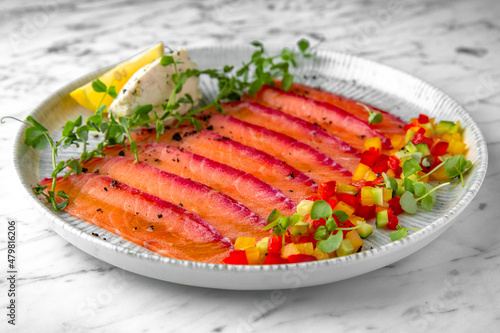 Lightly salted salmon, colored with beetroot juice with finely chopped fresh vegetables in a festive plate on a marble background. Restaurant banquet menu.