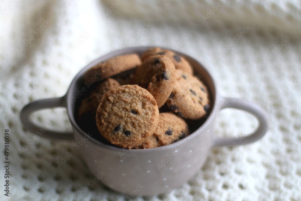 Bowl of chocolate chip cookies and soft knitted blanket. Hygge at home. Selective focus.