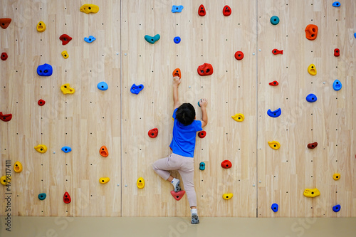 Foto Little boy climbing a rock wall indoor.