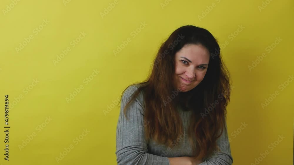 A beautiful shy woman with dark hair in a gray dress with dark hair shows shyness and coquetry. Pretty modest emotional woman on a yellow background. A beautiful shy woman with dark hair in a gray dress with dark hair shows shyness and coquetry. Pretty modest emotional woman on a yellow background.