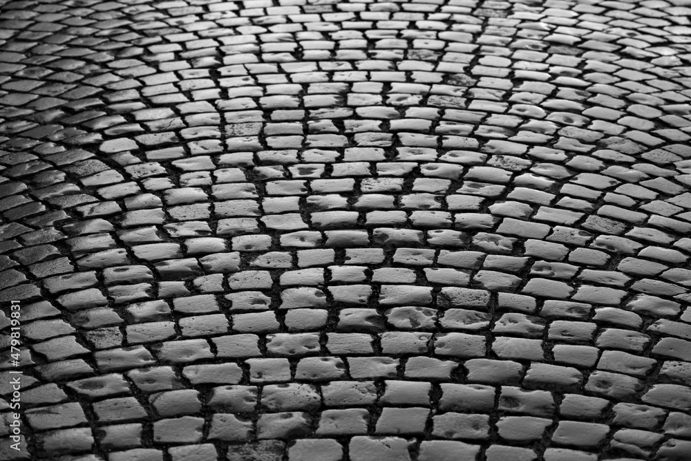 Old cobblestone street in Iserlohn Sauerland Germany. Wet shiny historic basalt ashlars and blocks reflecting sunshine after rain.  Pavement background, black and white greyscale with high contrast.
