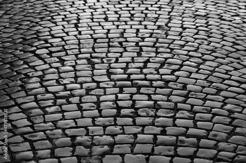 Old cobblestone street in Iserlohn Sauerland Germany. Wet shiny historic basalt ashlars and blocks reflecting sunshine after rain. Pavement background, black and white greyscale with high contrast.
