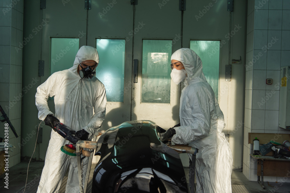 Workman in protective suit polishing car part near colleague in service. Workman in protective suit polishing car part near colleague in service.