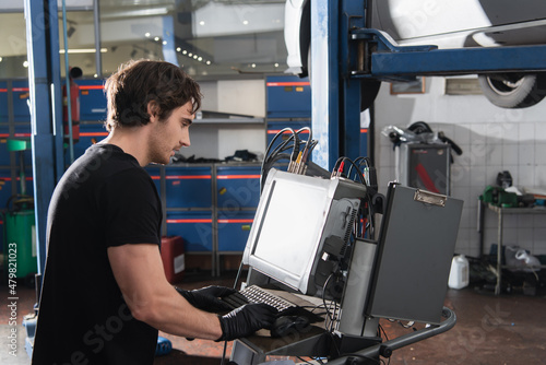 Side view of mechanic in gloves using computer in car service.