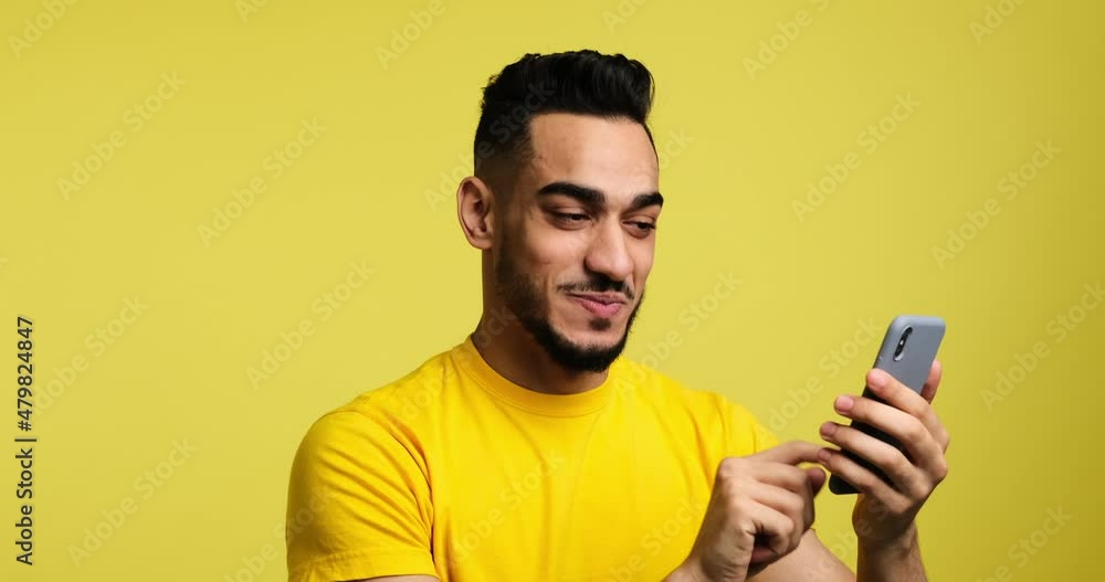 Happy man text messaging using mobile phone over yellow background Happy man text messaging using mobile phone over yellow background