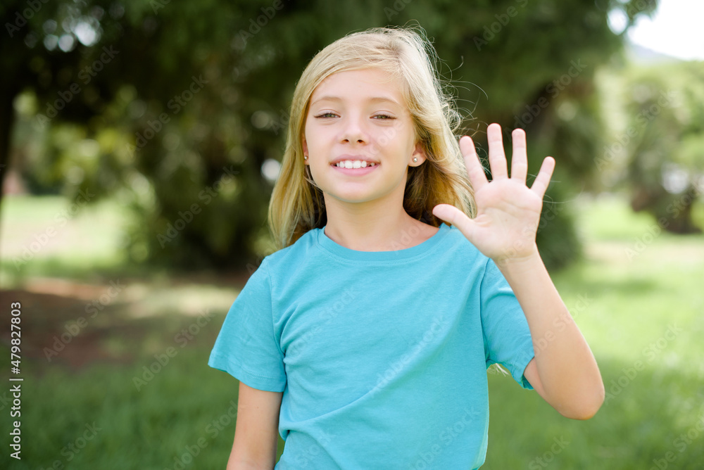 Caucasian little kid girl wearing blue T-shirt standing outdoors showing and pointing up with fingers number five while smiling confident and happy. Caucasian little kid girl wearing blue T-shirt standing outdoors showing and pointing up with fingers number five while smiling confident and happy.