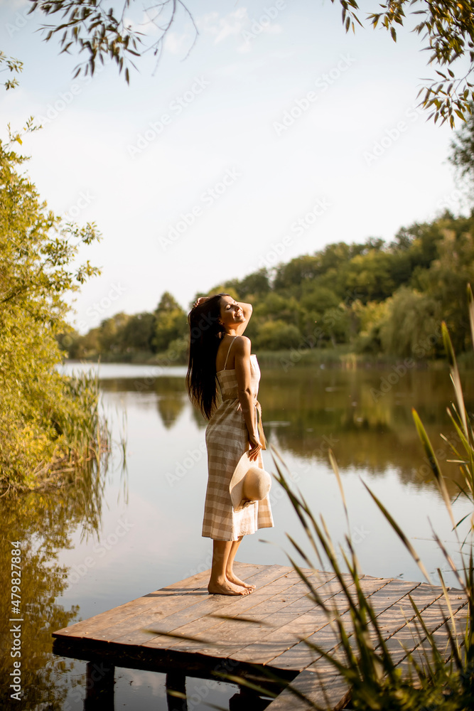 Young woman standing on the wooden pier at the calm lake