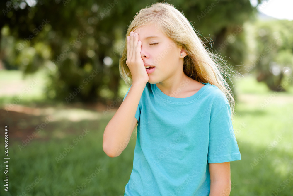 Caucasian little kid girl wearing blue T-shirt standing outdoors Yawning tired covering half face, eye and mouth with hand. Face hurts in pain. Caucasian little kid girl wearing blue T-shirt standing outdoors Yawning tired covering half face, eye and mouth with hand. Face hurts in pain.