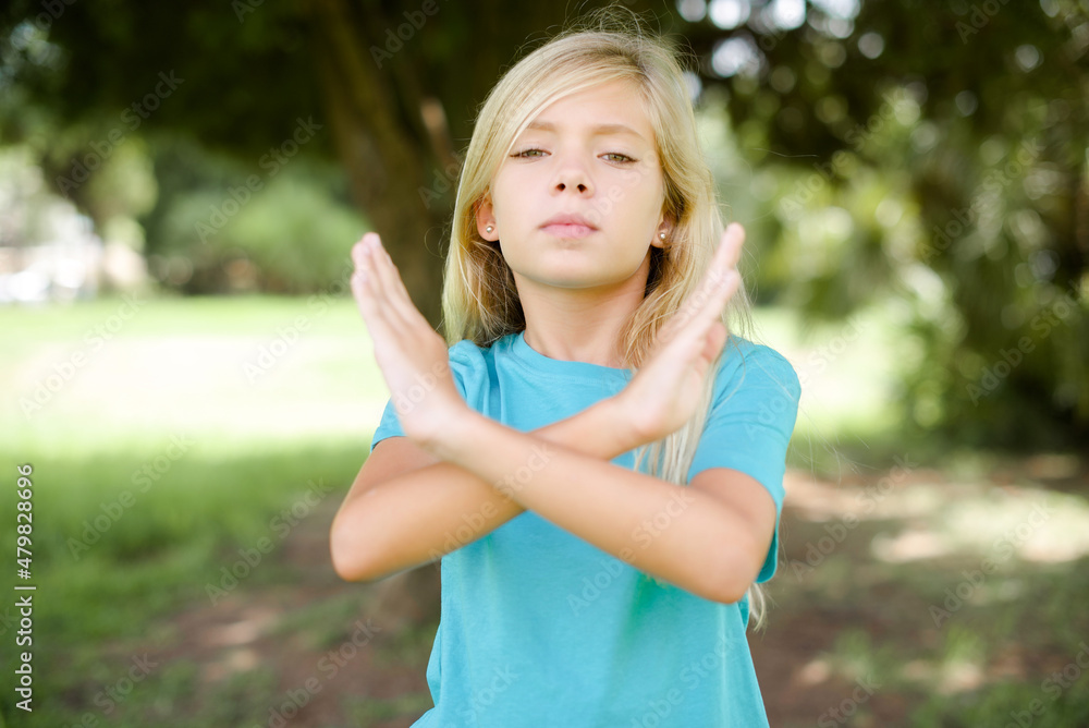 Caucasian little kid girl wearing blue T-shirt standing outdoors Rejection expression crossing arms doing negative sign, angry face Caucasian little kid girl wearing blue T-shirt standing outdoors Rejection expression crossing arms doing negative sign, angry face