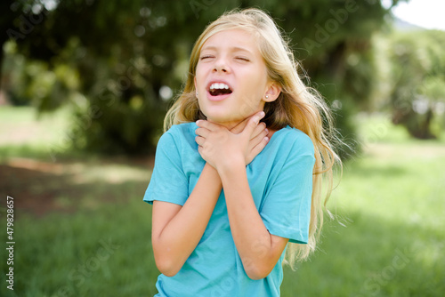 Fototapeta Caucasian little kid girl wearing blue T-shirt standing outdoors shouting suffocate because painful strangle