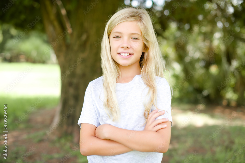 Self confident serious calm Caucasian little kid girl wearing white T-shirt standing outdoors stands with arms folded. Shows professional vibe stands in assertive pose. Self confident serious calm Caucasian little kid girl wearing white T-shirt standing outdoors stands with arms folded. Shows professional vibe stands in assertive pose.