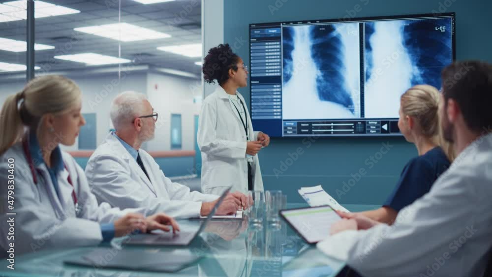 Hospital Conference Meeting Room: Young Promising Black Female Physician Presents Patient X-ray on TV Screen, Team of Doctors Discuss Treatment. Research Scientists and Drug, Medicine Development Hospital Conference Meeting Room: Young Promising Black Female Physician Presents Patient X-ray on TV Screen, Team of Doctors Discuss Treatment. Research Scientists and Drug, Medicine Development