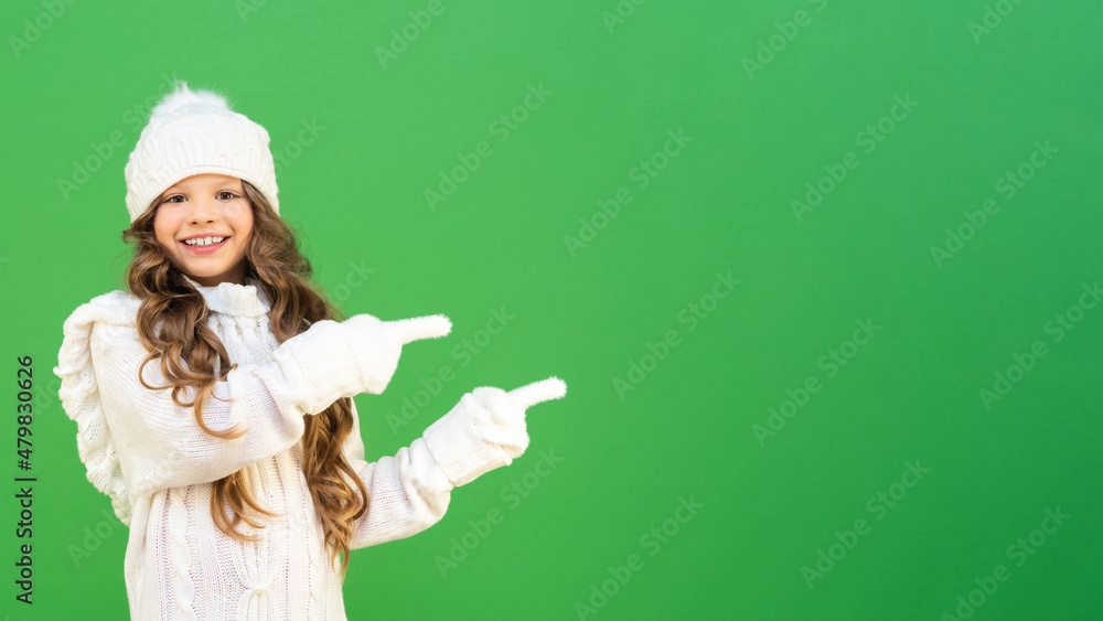 A beautiful model in a warm knitted sweater points to the advertisement and smiles. baby model in warm winter clothes on a green isolated background with copying space. A beautiful model in a warm knitted sweater points to the advertisement and smiles. baby model in warm winter clothes on a green isolated background with copying space.