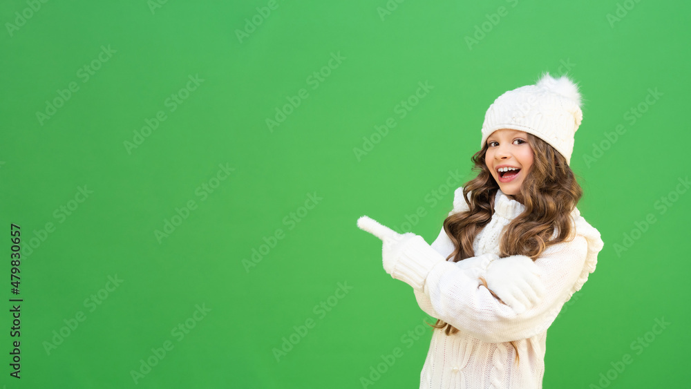 A beautiful model in a warm knitted sweater points to the advertisement and smiles. baby model in warm winter clothes on a green isolated background with copying space. A beautiful model in a warm knitted sweater points to the advertisement and smiles. baby model in warm winter clothes on a green isolated background with copying space.