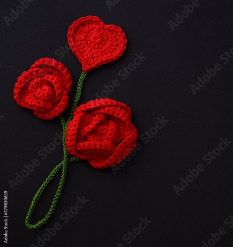 Crocheted red roses and heart on black background close up. 