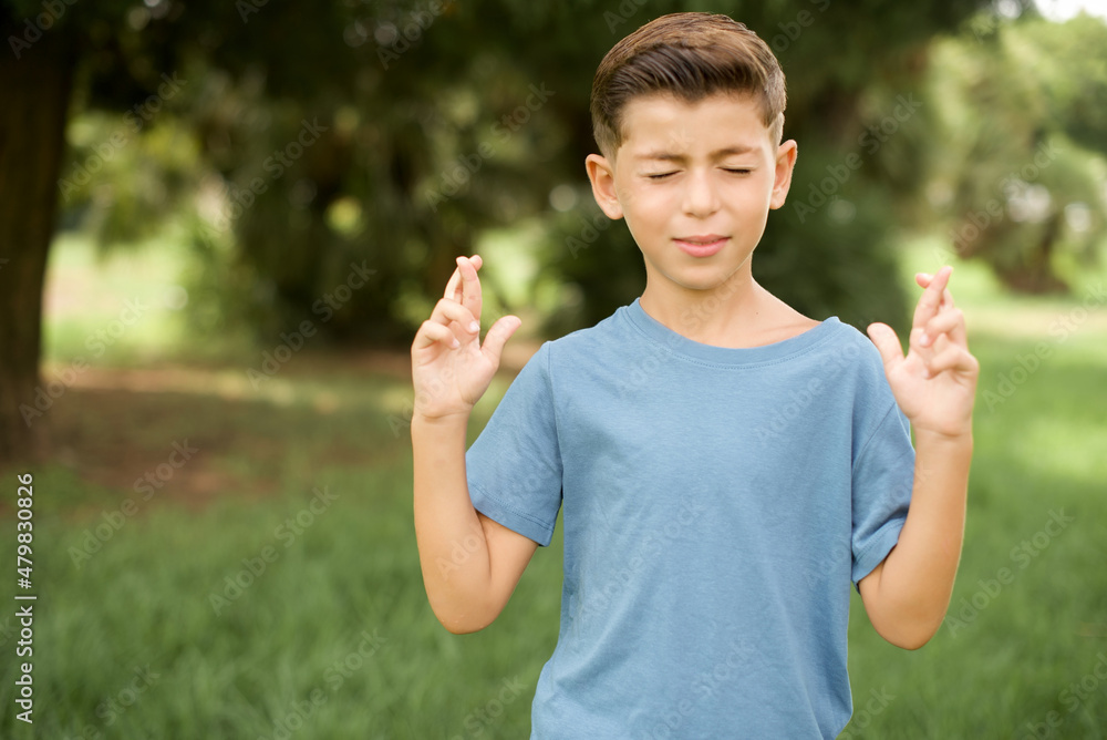 beautiful Caucasian little kid boy wearing yellow T-shirt standing outdoors has big hope, crosses fingers, believes in good fortune, smiles broadly. People and wish concept beautiful Caucasian little kid boy wearing yellow T-shirt standing outdoors has big hope, crosses fingers, believes in good fortune, smiles broadly. People and wish concept