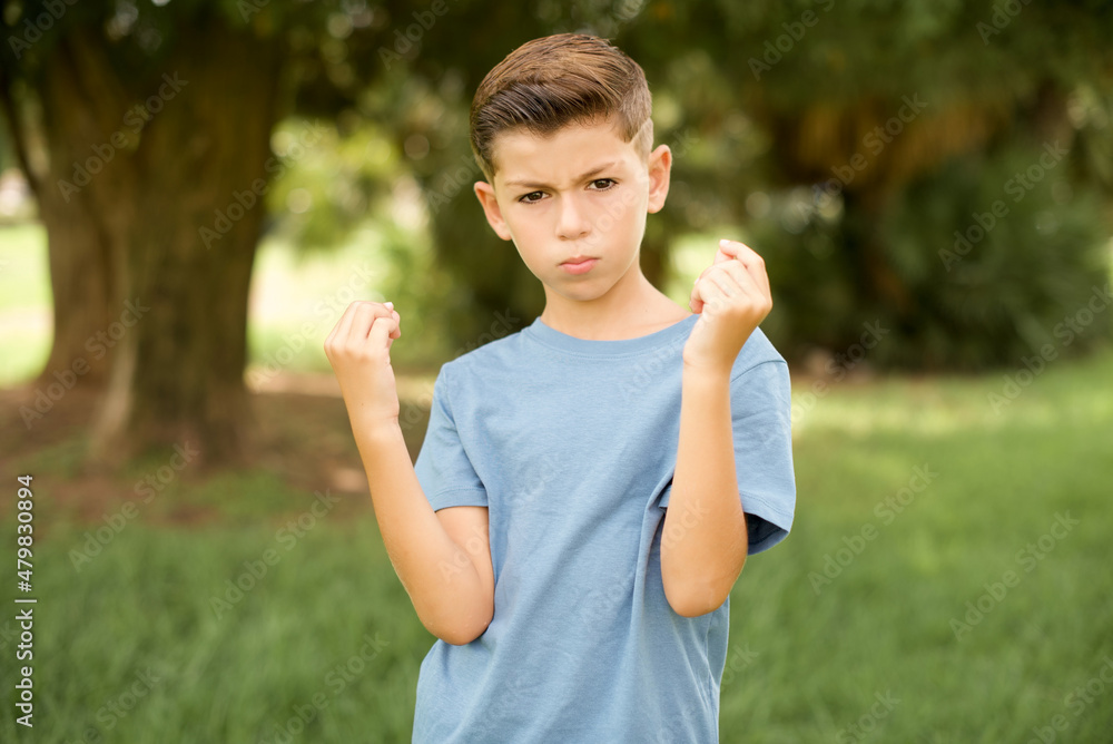 beautiful Caucasian little kid boy wearing blue T-shirt standing outdoors doing money gesture with hands, asking for salary payment, millionaire business beautiful Caucasian little kid boy wearing blue T-shirt standing outdoors doing money gesture with hands, asking for salary payment, millionaire business