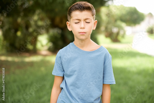 beautiful Caucasian little kid boy wearing blue T-shirt standing outdoors looking sleepy and tired, exhausted for fatigue and hangover, lazy eyes in the morning.