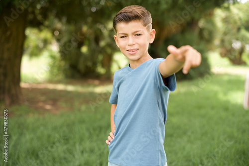 beautiful Caucasian little kid boy wearing blue T-shirt standing outdoors pointing at camera with a satisfied  confident  friendly smile  choosing you