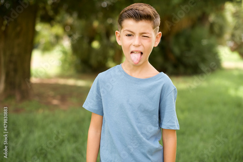 beautiful Caucasian little kid boy wearing blue T-shirt standing outdoors winking looking at the camera with sexy expression, cheerful and happy face.