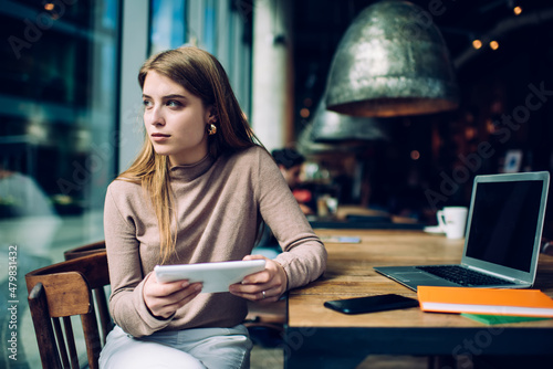 Young serious female student looking out window while sitting in time cafe