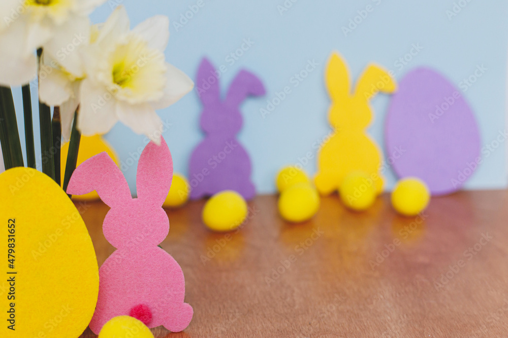 Colorful Easter bunnies, eggs and daffodils bouquet on table against blue background with space for text. Happy Easter! Purple, yellow, pink artificial decor and spring flowers. Easter hunt Colorful Easter bunnies, eggs and daffodils bouquet on table against blue background with space for text. Happy Easter! Purple, yellow, pink artificial decor and spring flowers. Easter hunt