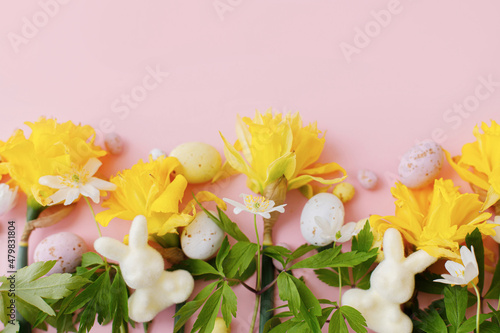 Happy Easter! Colorful Easter chocolate eggs, bunnies and daffodils flowers border on pink background. Stylish Easter flat lay. Greeting card or banner template