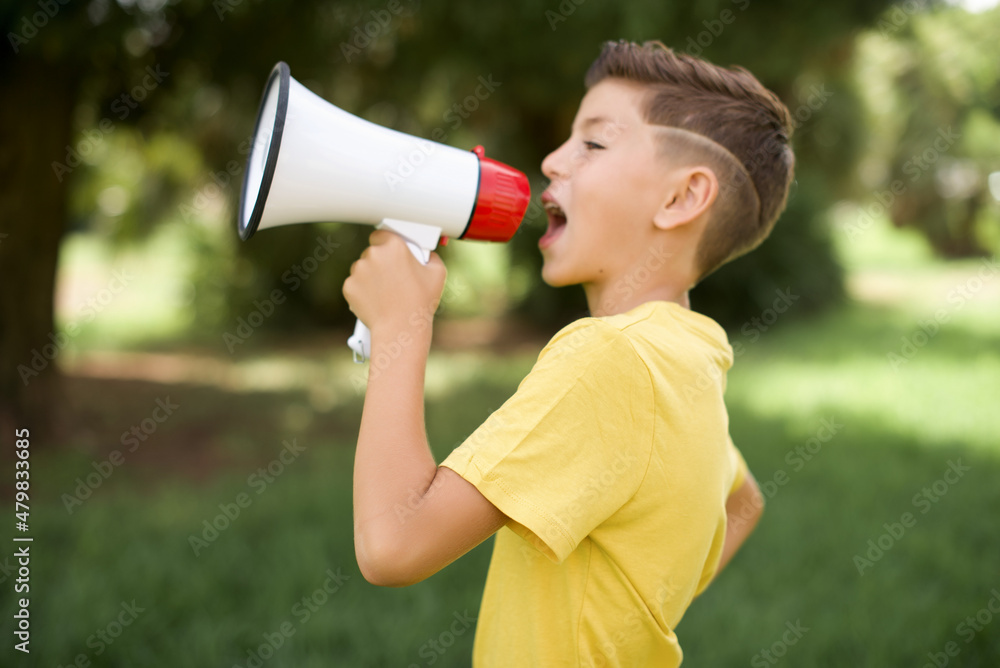 Funny Caucasian little kid boy wearing yellow T-shirt standing outdoors People sincere emotions lifestyle concept. Mock up copy space. Screaming in megaphone. Funny Caucasian little kid boy wearing yellow T-shirt standing outdoors People sincere emotions lifestyle concept. Mock up copy space. Screaming in megaphone.