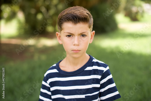 Stunned Caucasian little kid boy wearing stripped T-shirt standing outdoors stares reacts on shocking news. Astonished boy holds breath
