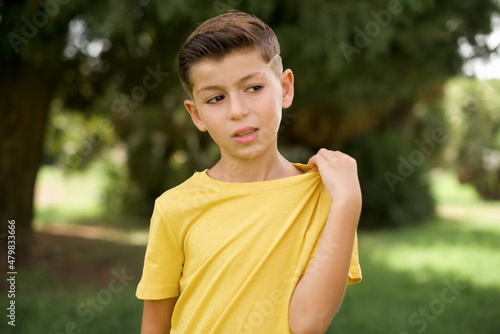 Caucasian little kid boy wearing yellow T-shirt standing outdoors stressed, anxious, tired and frustrated, pulling shirt neck, looking frustrated with problem