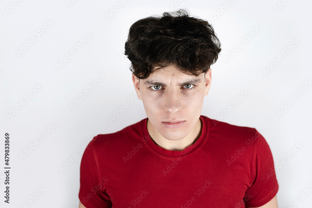 Portrait of a young guy with dark hair in a red T-shirt with angry emotions on his face, the guy is annoyed and sad, disappointed with the behavior of friends Portrait of a young guy with dark hair in a red T-shirt with angry emotions on his face, the guy is annoyed and sad, disappointed with the behavior of friends