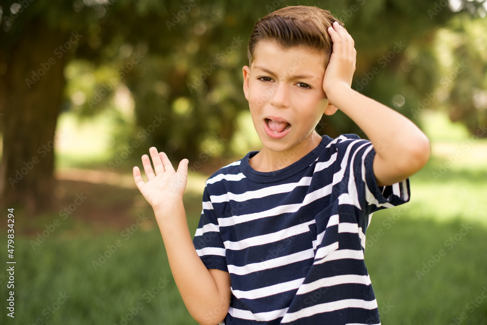 Shocked amazed surprised beautiful Caucasian little kid boy wearing stripped T-shirt standing outdoors hold hand offering proposition Shocked amazed surprised beautiful Caucasian little kid boy wearing stripped T-shirt standing outdoors hold hand offering proposition