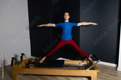 Sporty man doing exercises on pilates reformer training machine. Working out wearing sportswear, gym.