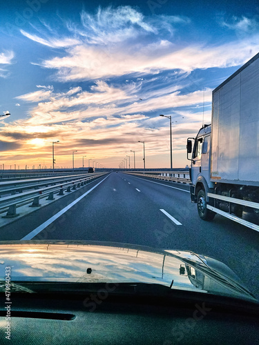 View from the car's windshield to a beautiful sunset, a large highway, a truck. Traveling by car. Beautiful blue-orange sky at sunset.