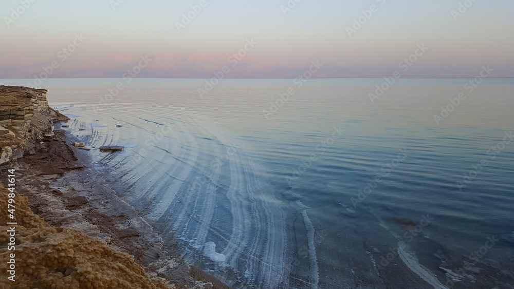 View of Dead Sea coastline. Salt crystals at sunset. Texture of Dead sea. Salty sea shore. Landscape Dead Sea coastline with natural relief channels in summer day,  failures of the soil