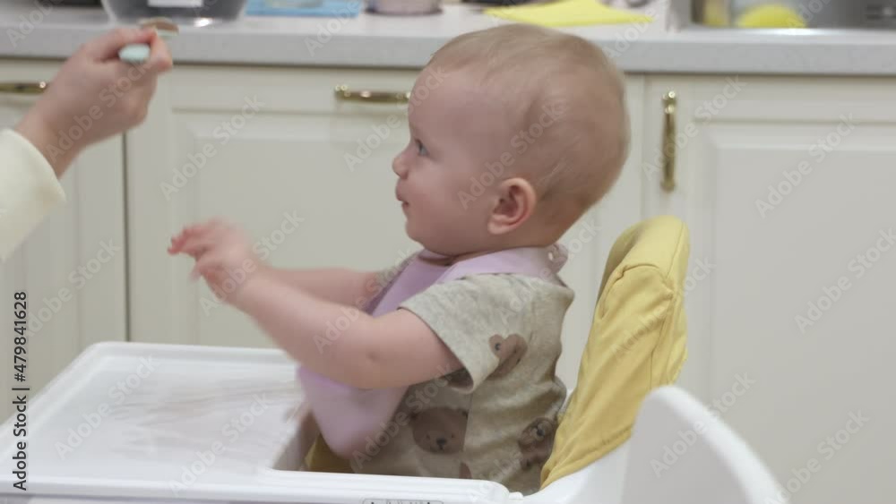 Mother feeding baby with spoon, 10 month old baby boy sitting on eating high chair. High quality 4k footage Mother feeding baby with spoon, 10 month old baby boy sitting on eating high chair. High quality 4k footage