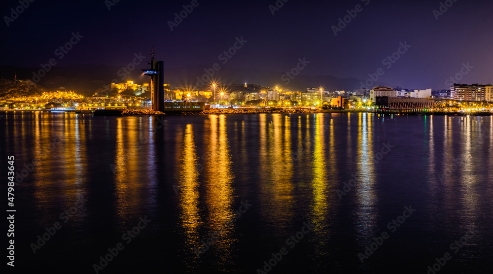 Skyline cityscape of Almeria at twilight from the lighthouse, Andalusia, Spain. Lights of metropolis shining in the seawater. Panorama.