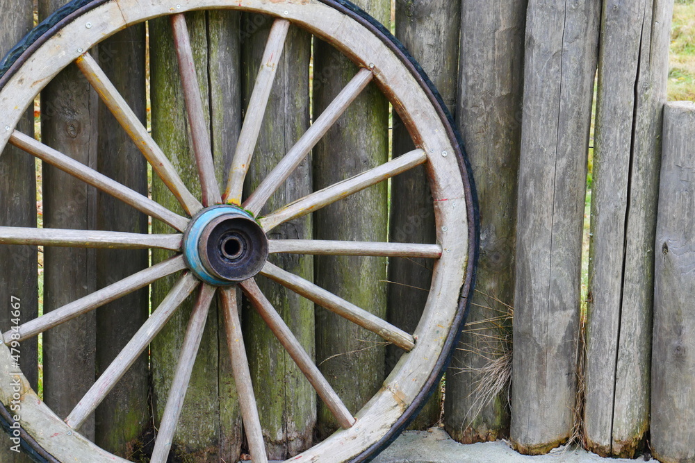 an old wooden wagon wheel from the wild west stands on a fence made of wooden stakes
